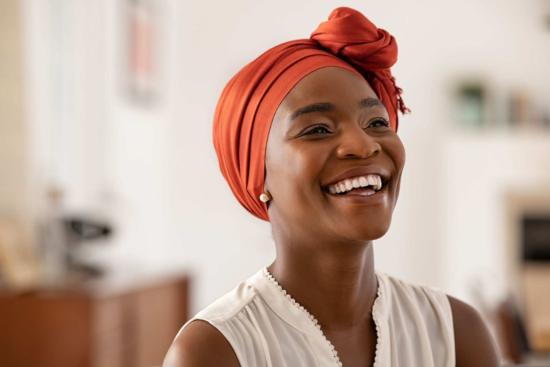 A woman wearing an orange head scarf is smiling.