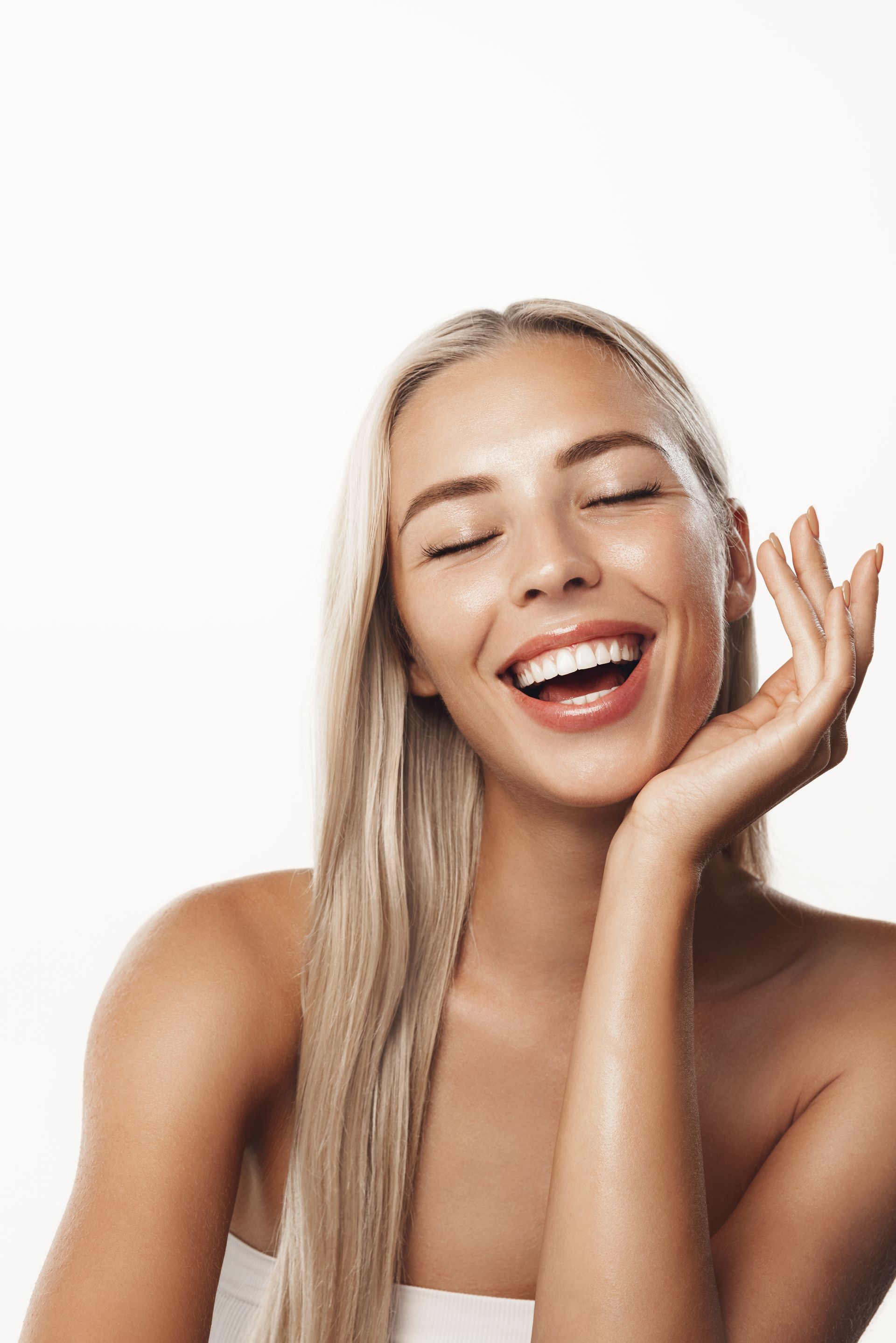 Woman with long blonde hair, eyes closed, smiling broadly, hand touching face.