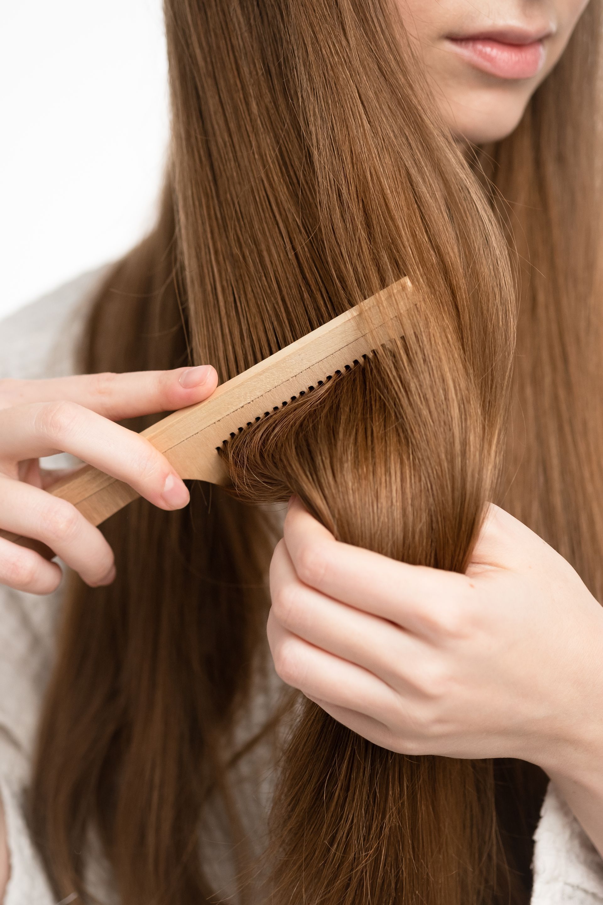 A woman is brushing her hair with a wooden comb.