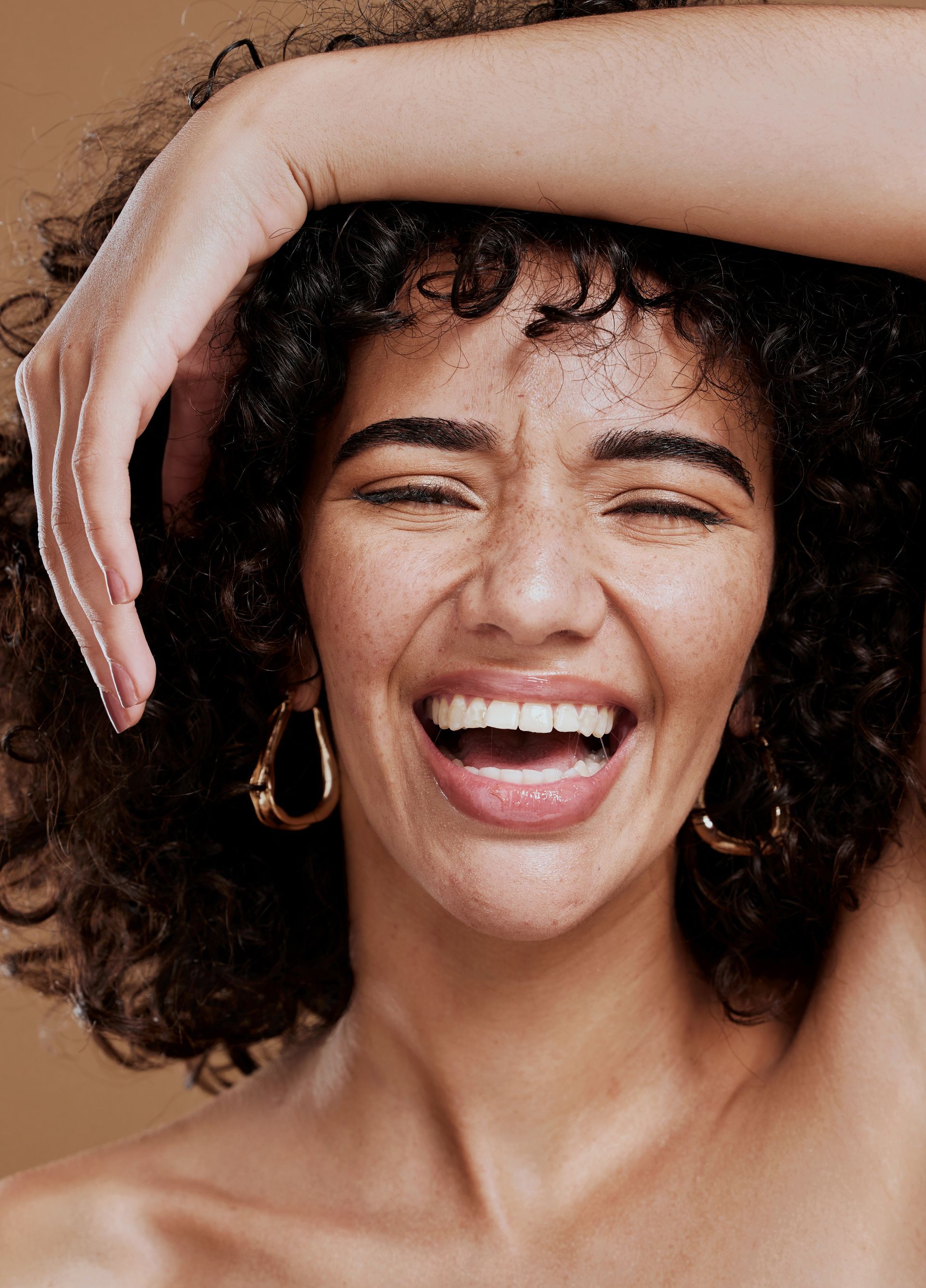 A woman with curly hair is laughing with her hand on her head.