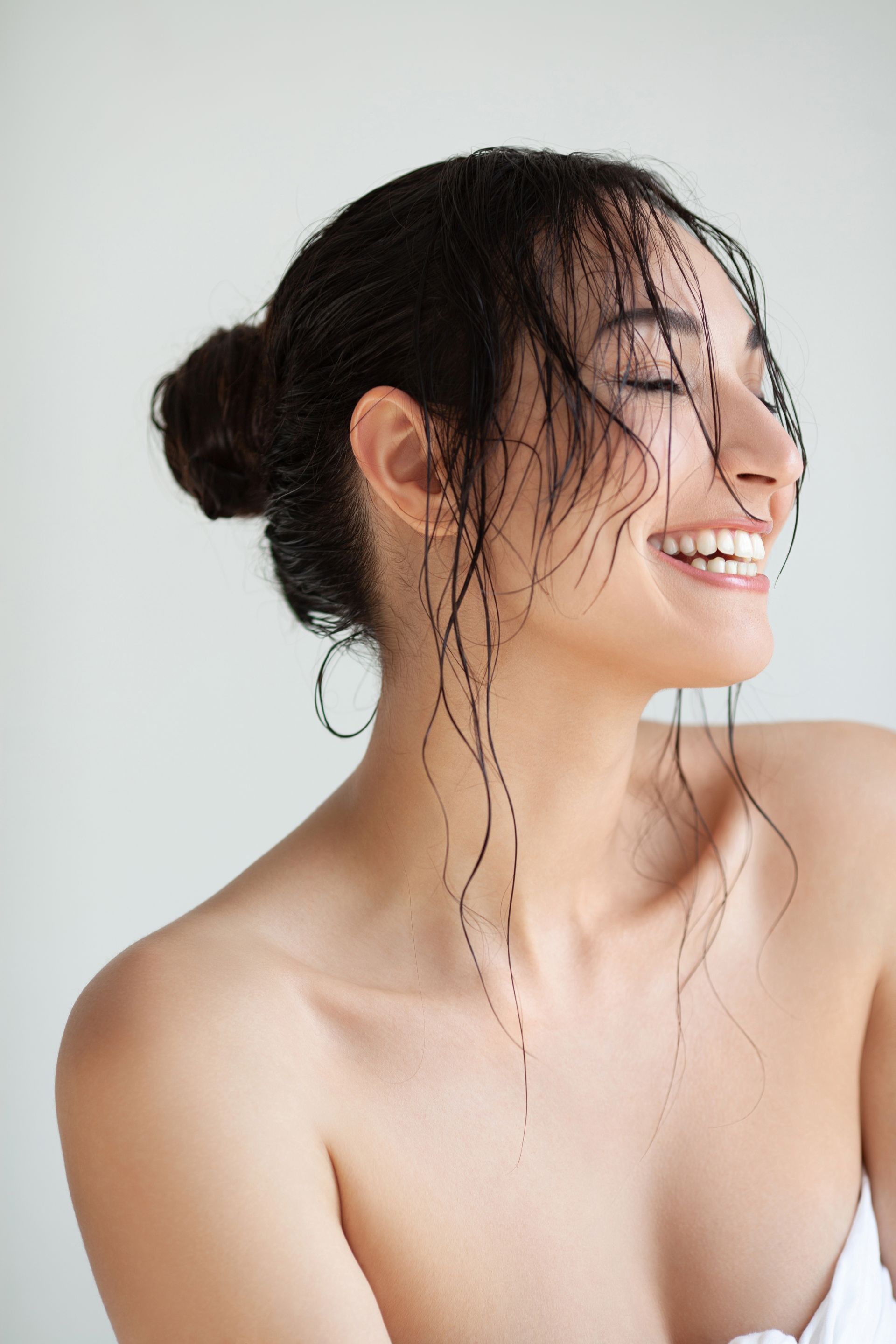 A woman with wet hair in a bun is smiling with her eyes closed.