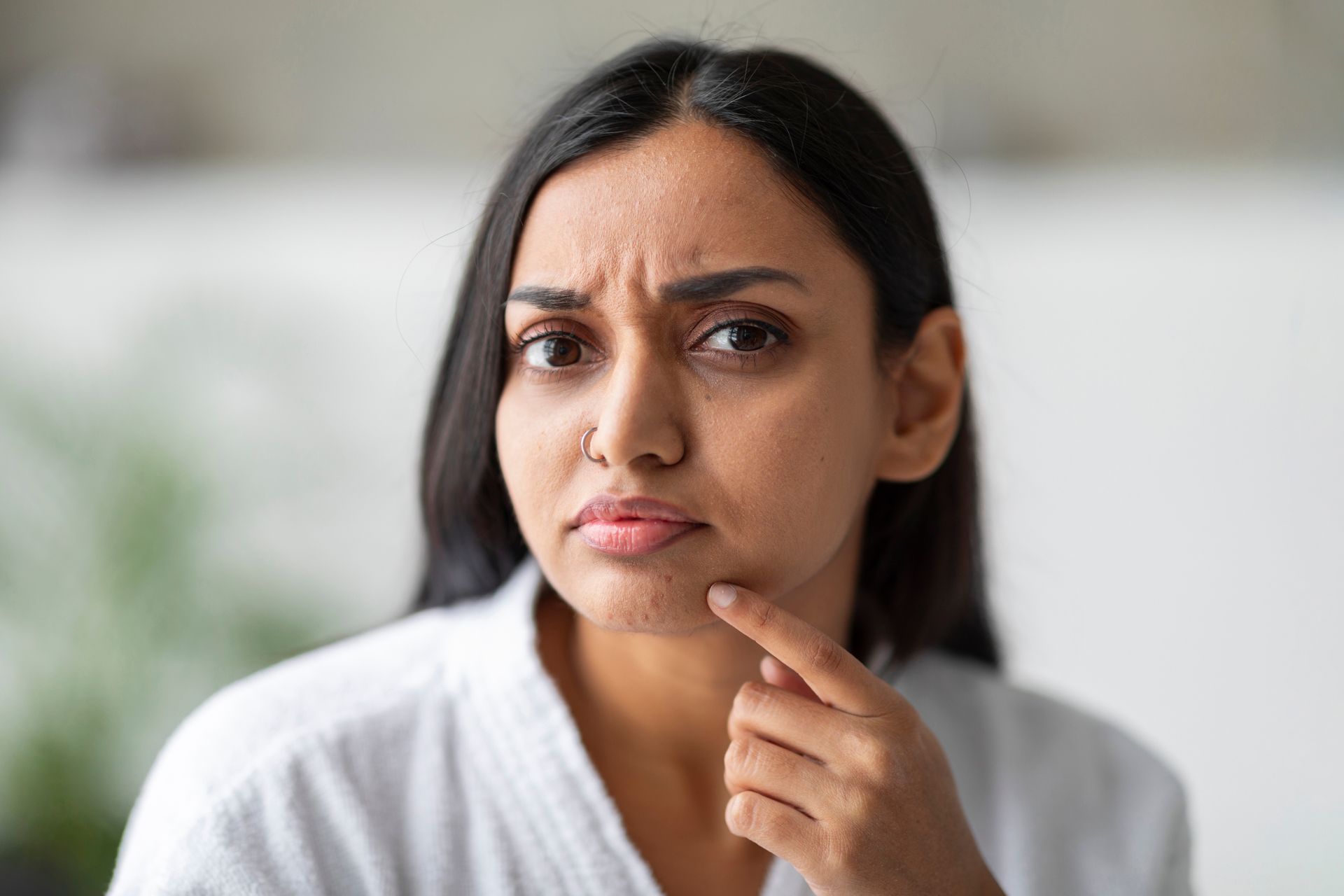 Woman touching her jaw, with a concerned expression, indoors.