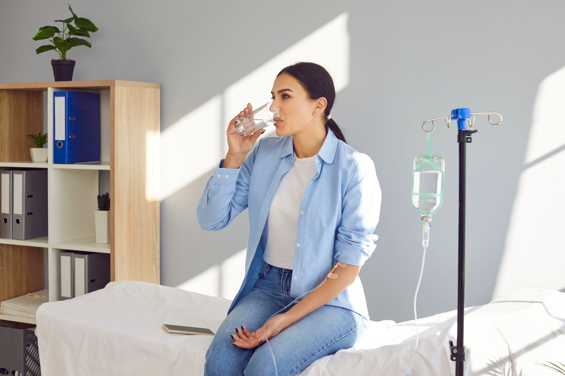 A woman is sitting on a bed drinking a glass of water.