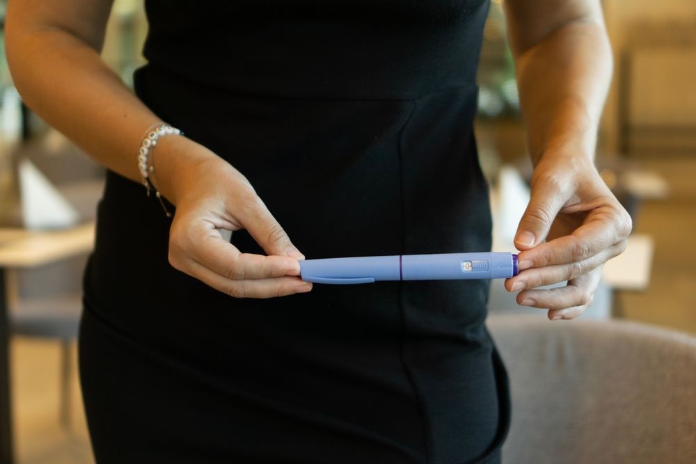 Woman in black dress holding a blue insulin pen.
