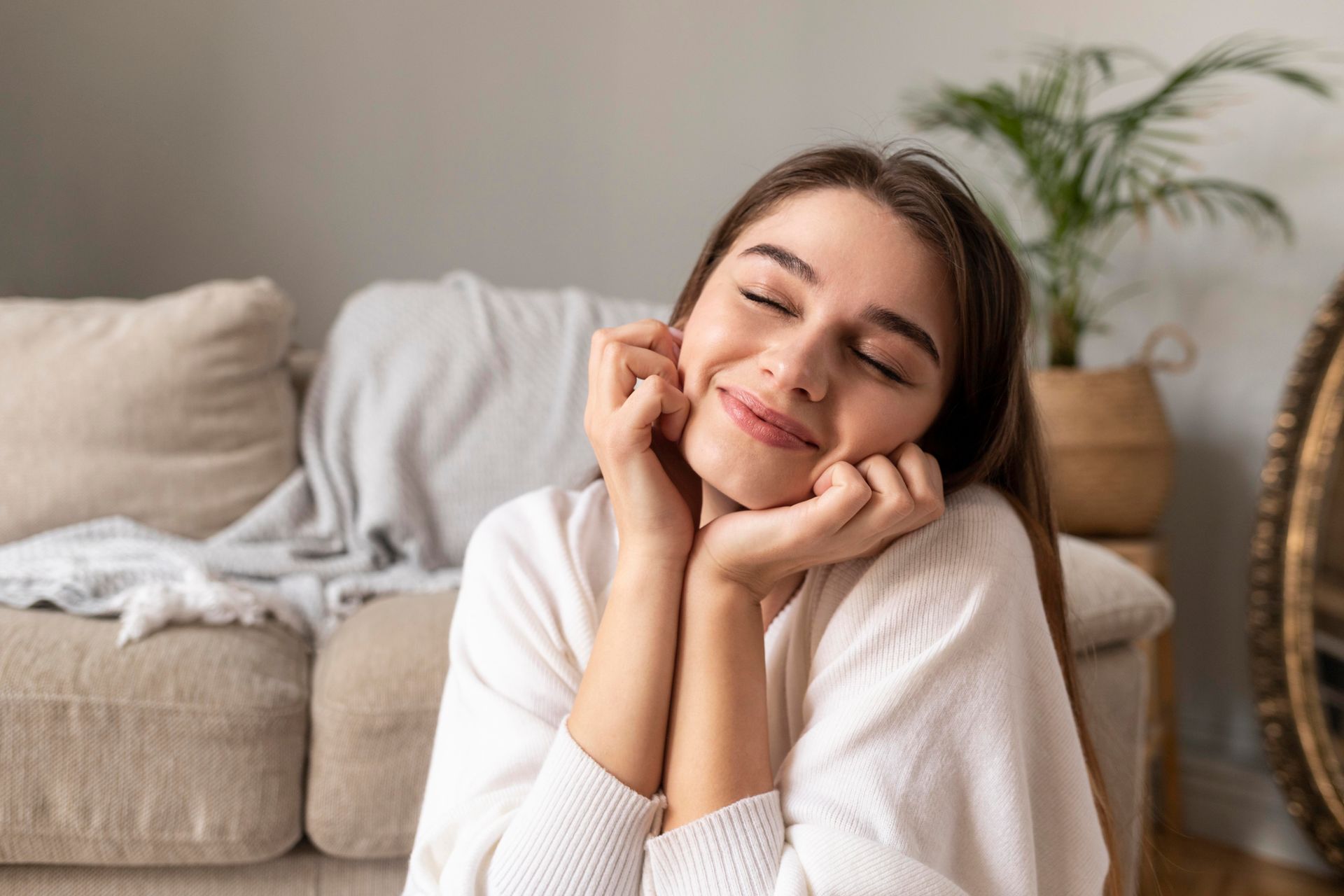 A woman is sitting on a couch with her eyes closed and her hands on her face.