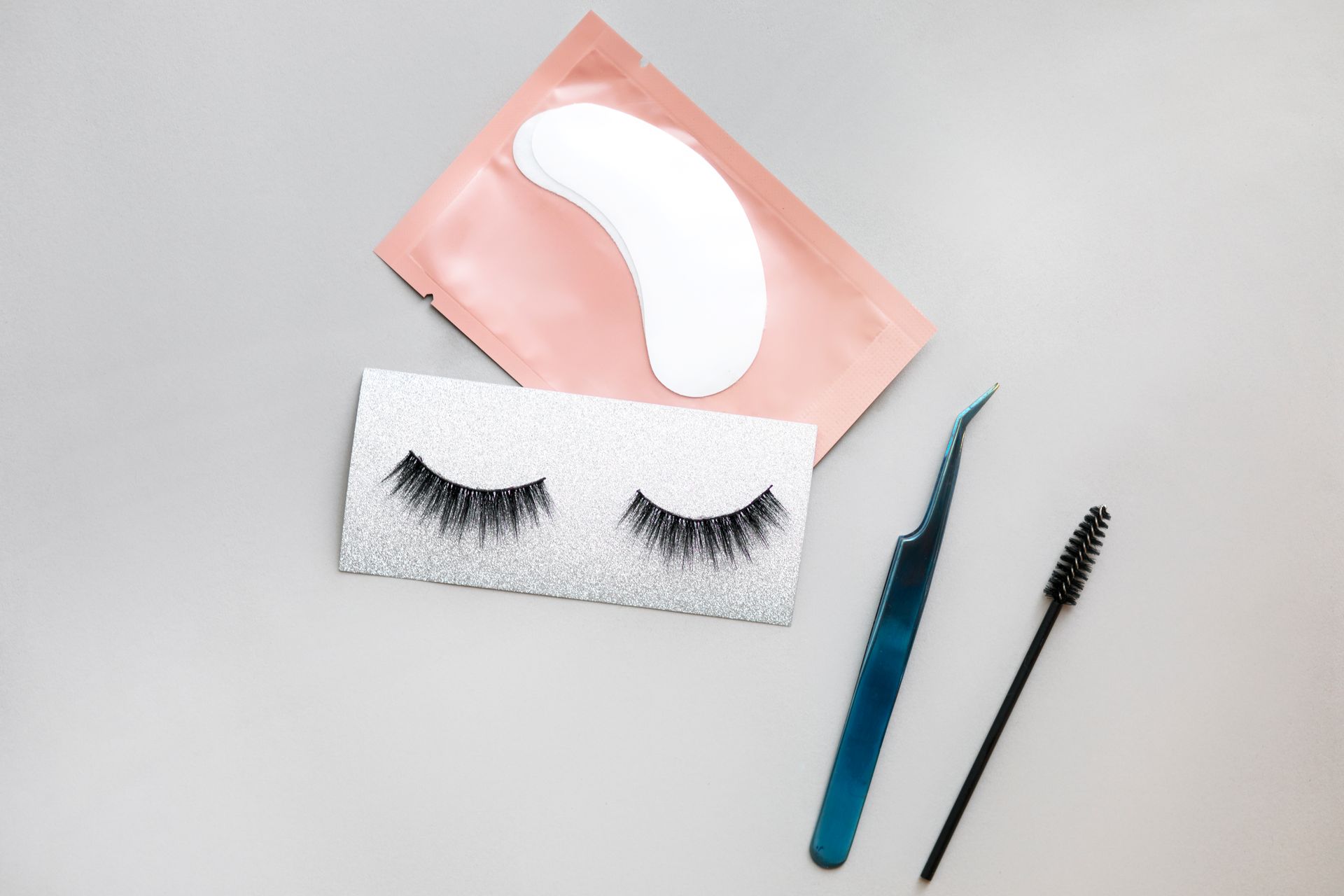 A pair of fake eyelashes , a pair of tweezers , and a mascara brush on a table.