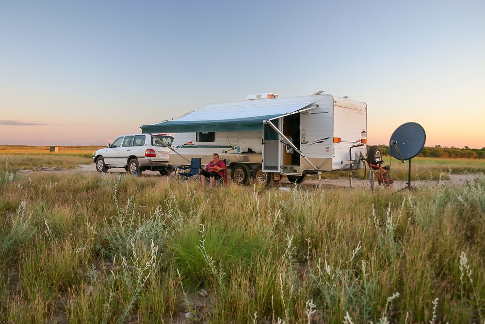 Rv Camper in a Grassy Field at Sunset With a Satellite Dish and Truck Nearby — Dempsters Caravan & RV in Gin Gin, QLD