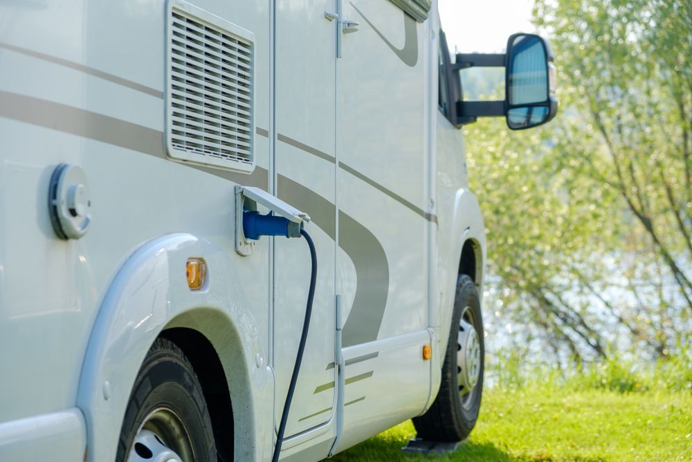 White Rv With Plugged-in Cable Parked on Grass Near Trees and Water — Dempsters Caravan & RV in Gin Gin, QLD