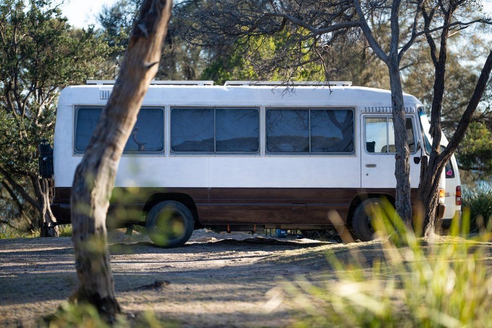 A White Bus is Parked in a Parking Lot Surrounded by Trees — Dempsters Caravan & RV in Rockhampton, QLD