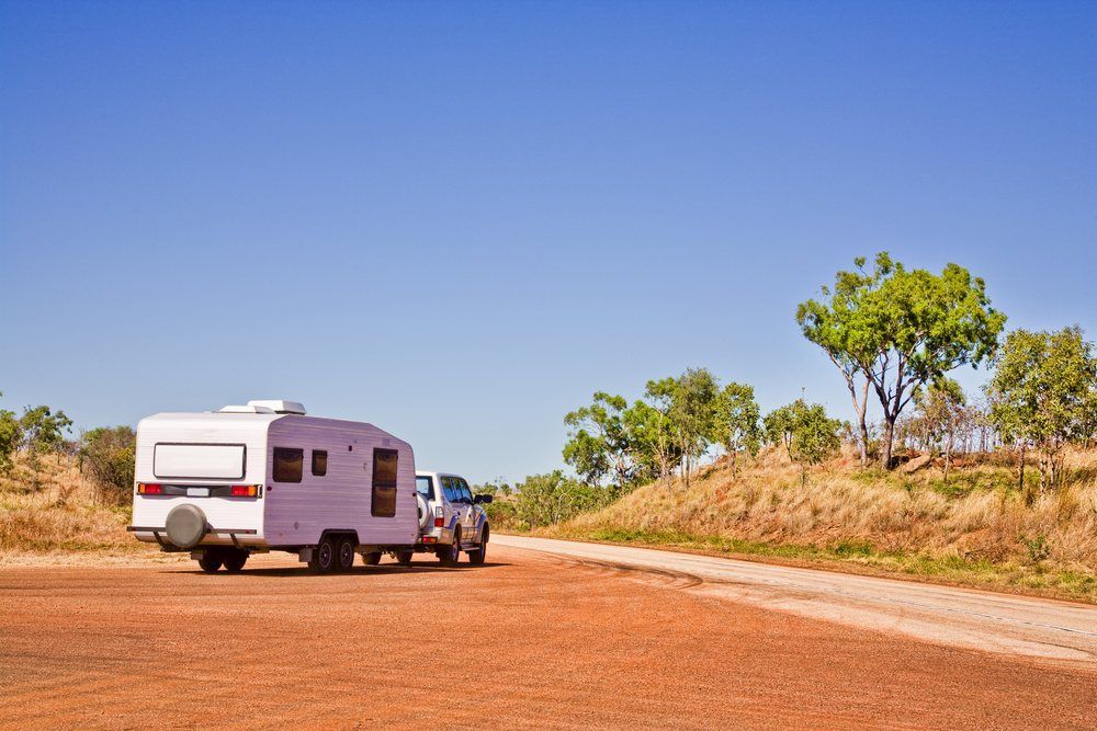 A White Rv is Towed by a Truck on a Dirt Road — Dempsters Caravan & RV in Rockhampton, QLD