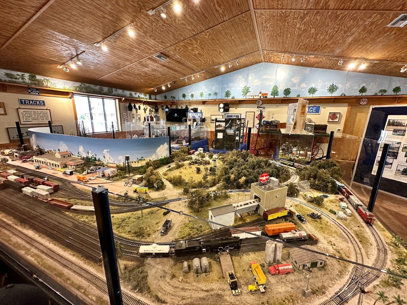 A detailed model train layout in a museum, featuring trains, buildings, and a landscape under a light-colored ceiling.