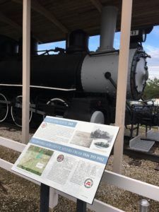 A black and white train is sitting under a wooden structure with a sign in front of it.