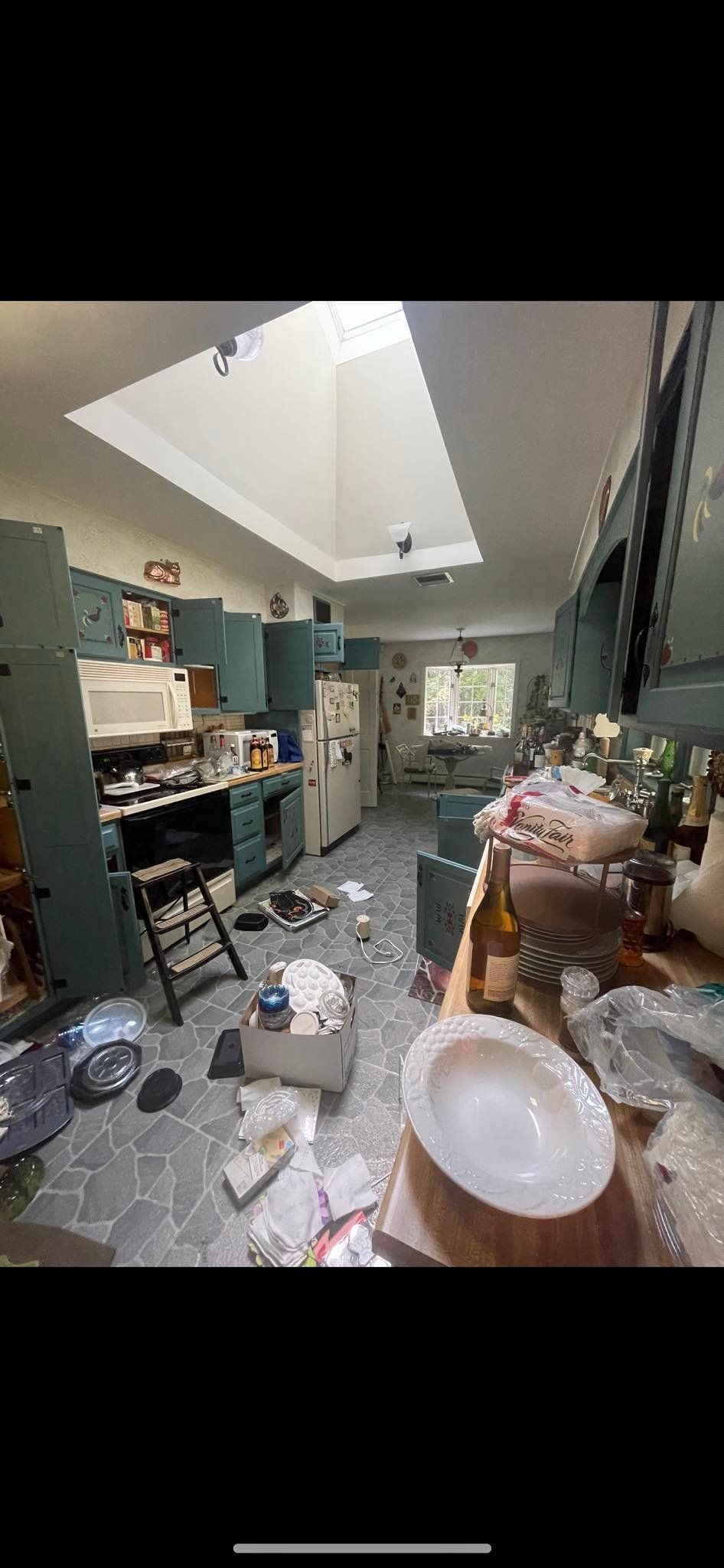 A cluttered kitchen with dark green cabinets, a skylight, and various items scattered across the floor and countertops.
