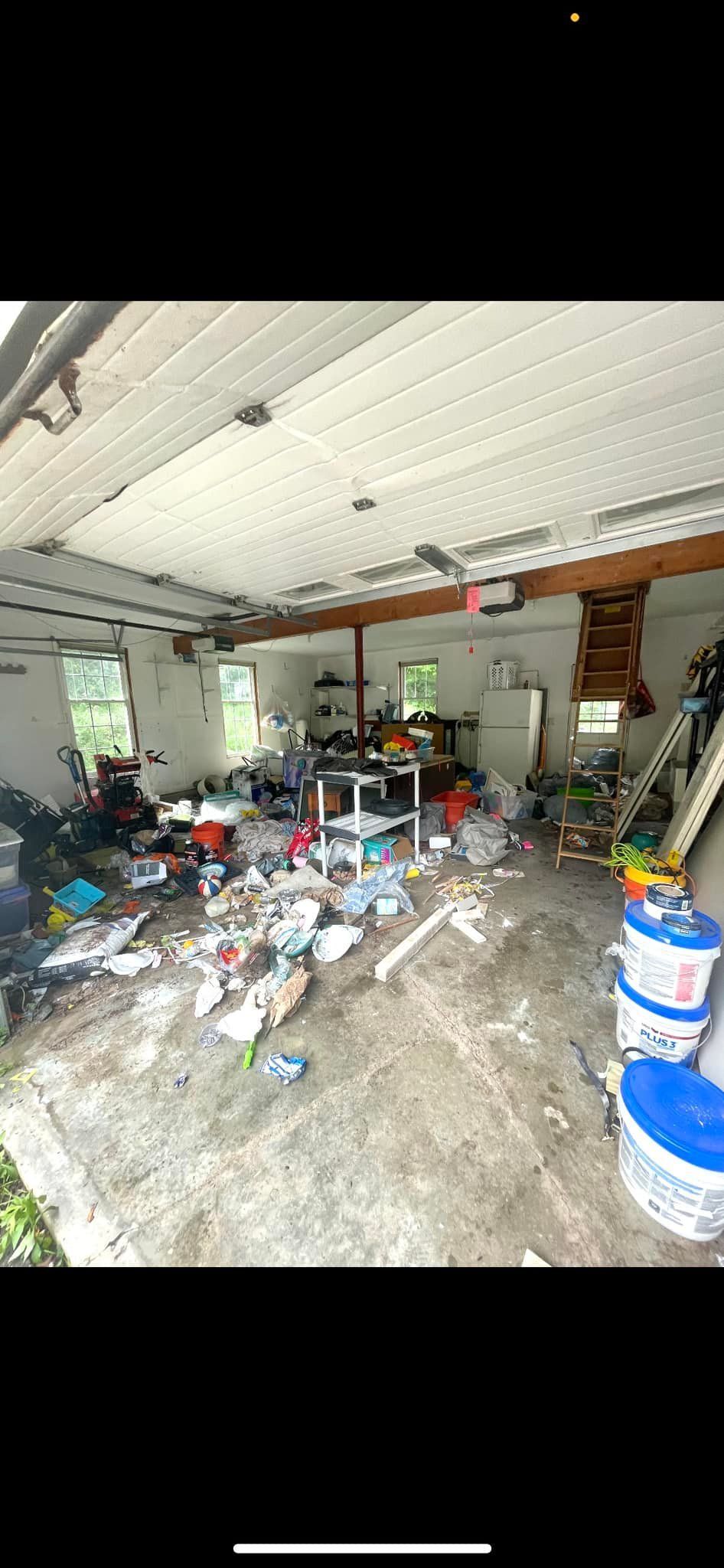 A cluttered, messy garage interior with white walls, a metal ceiling, and debris scattered across the concrete floor.