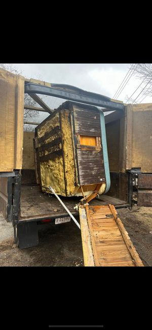 A dilapidated, partially dismantled wooden shed structure sits inside the back of a truck, connected to a wooden ramp.
