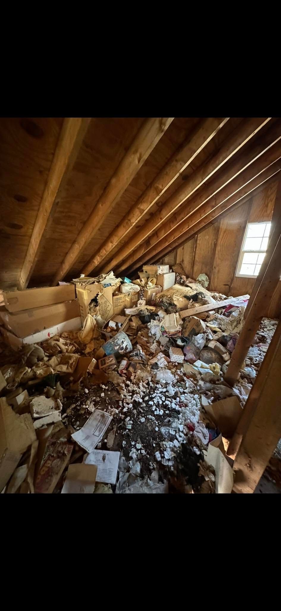 An unfinished attic space cluttered with loose debris, cardboard boxes, and piles of discarded materials.