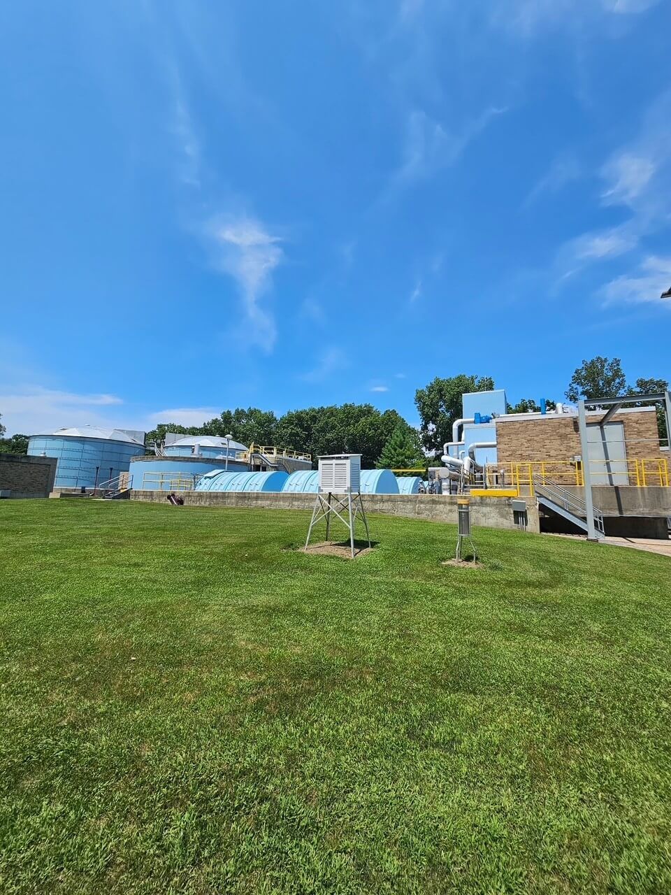 Grassy field with blue-and-white buildings and a bright blue sky.