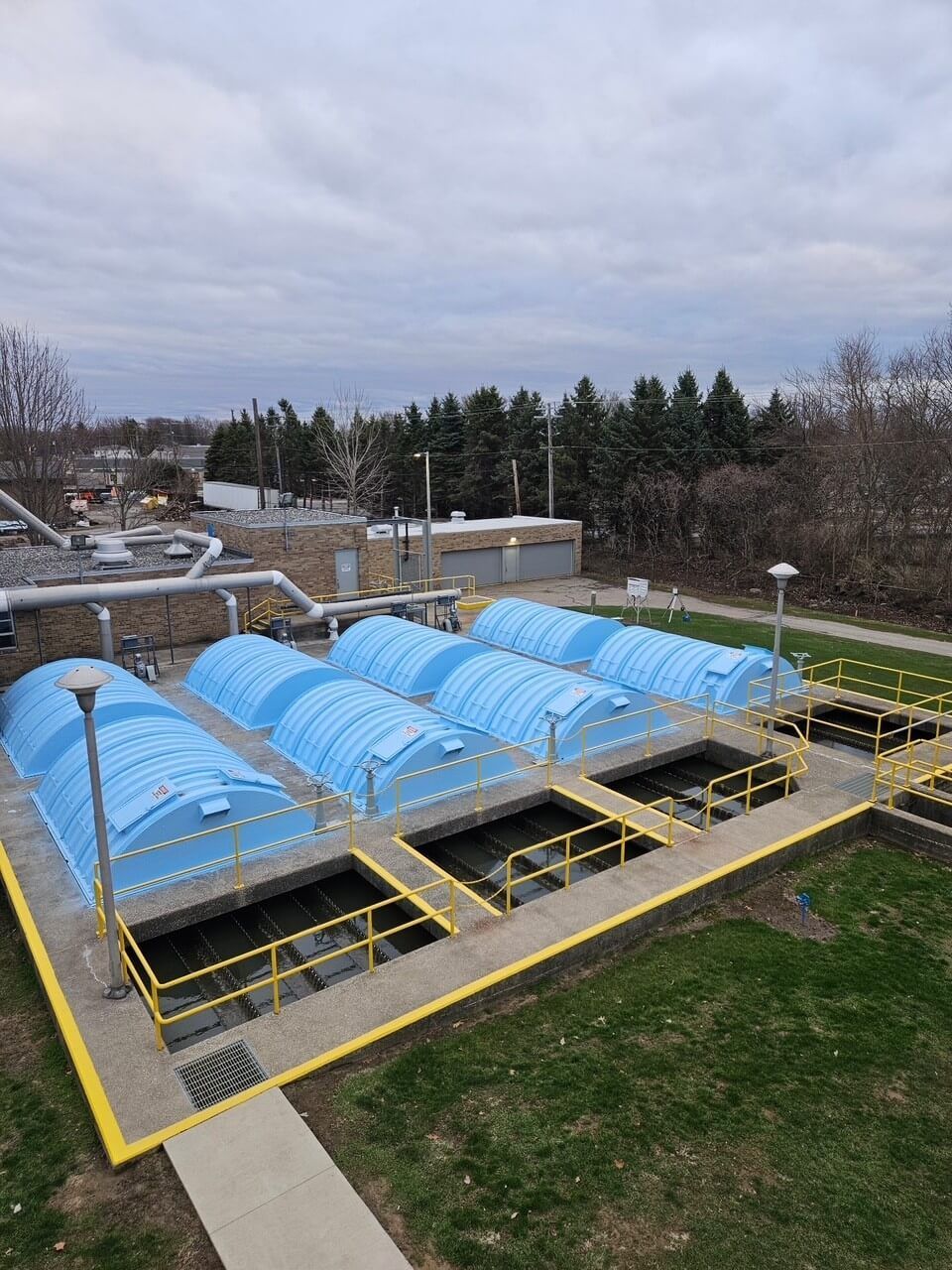 Blue arched greenhouse tunnels in a fenced outdoor garden on an overcast day.