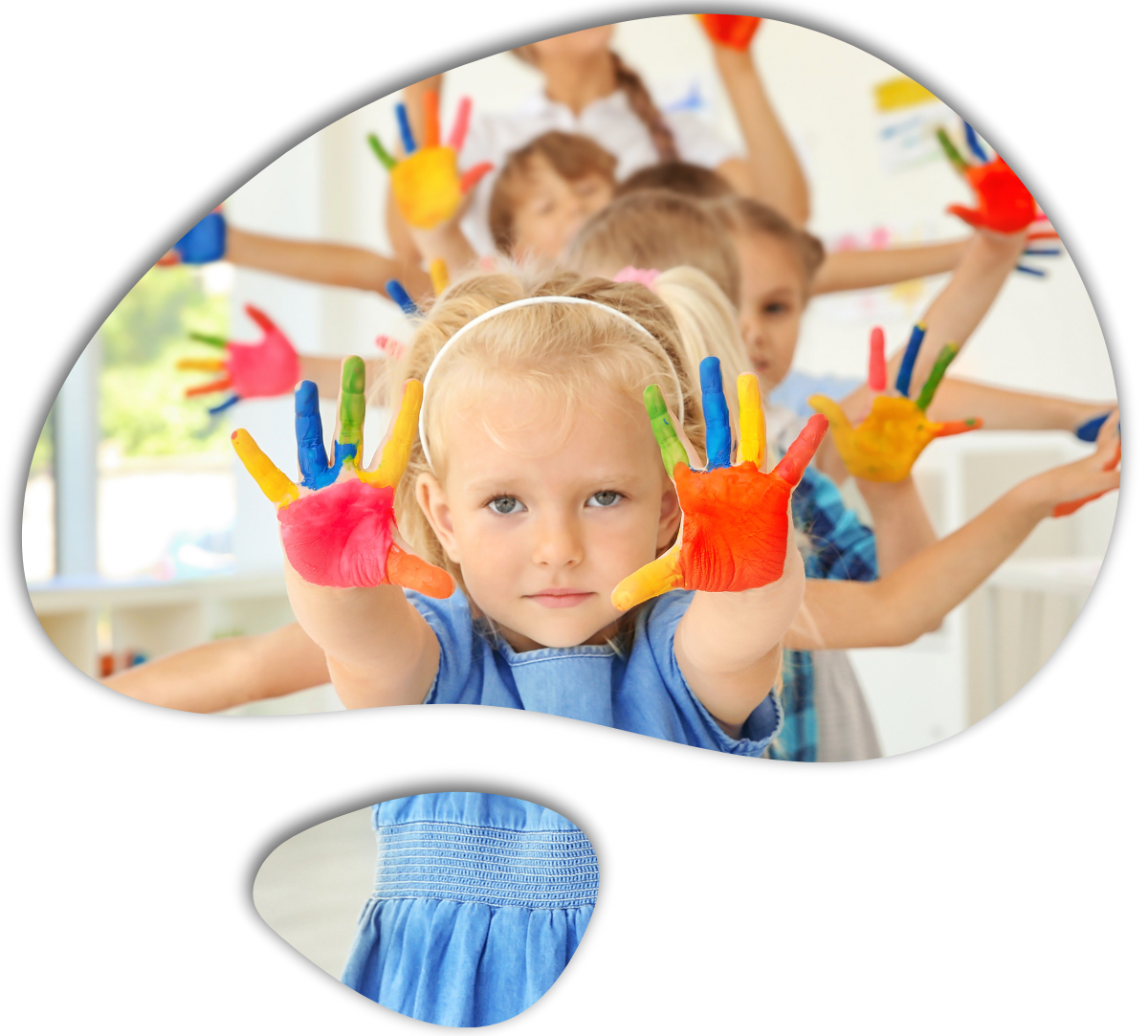A group of children in a classroom hold up their hands, which are covered in bright, multi-colored paint.
