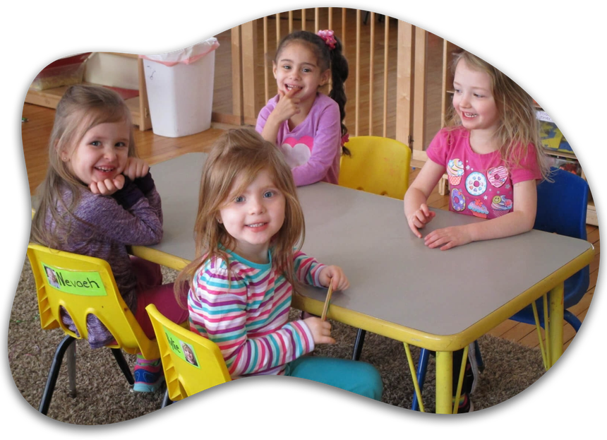 Four little girls are sitting at a table with one of them wearing a shirt that says pooh