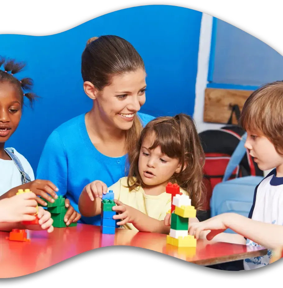 A woman is sitting at a table with children playing with blocks.