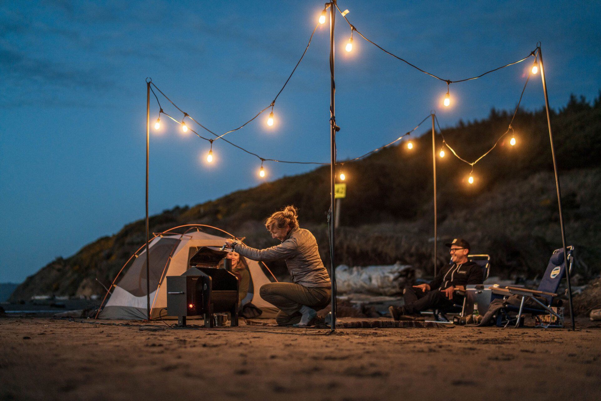 A man and a woman are camping on the beach at night.