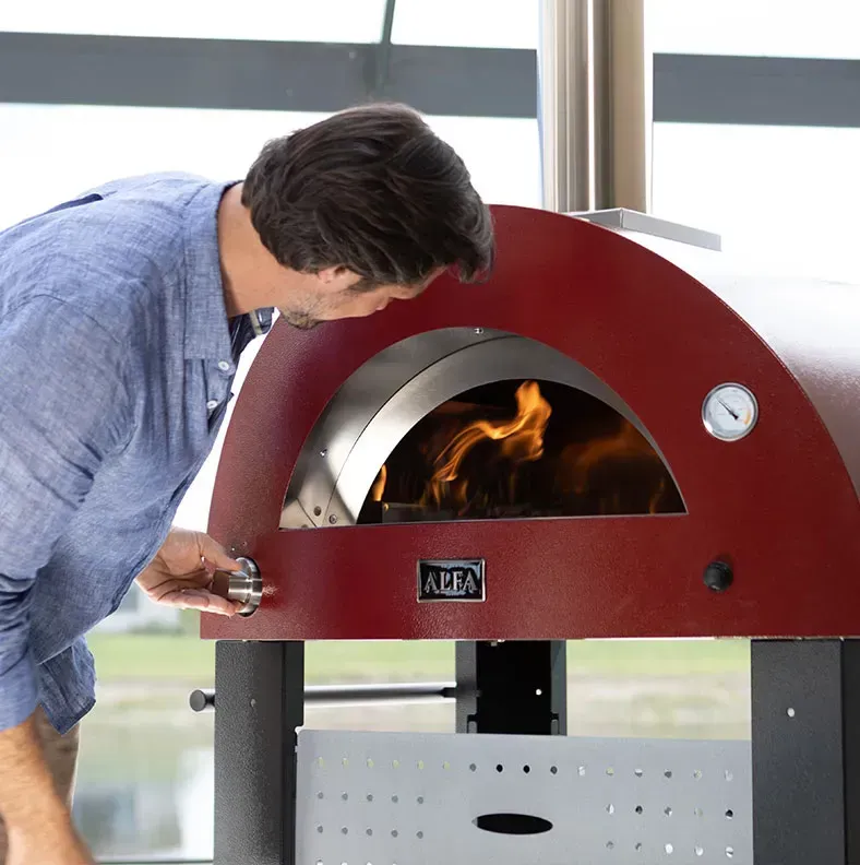 a man looks into a red alfa pizza oven