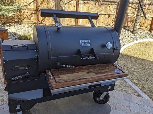 A large black grill with a wooden cutting board on top of it.