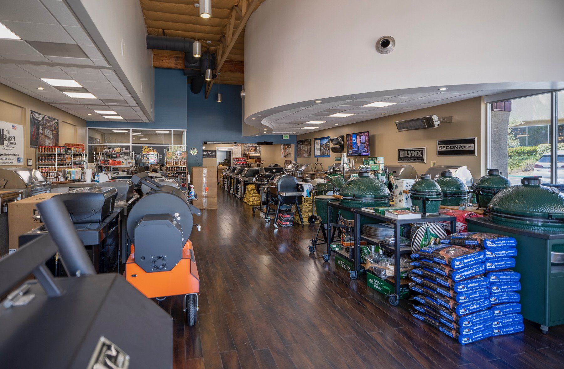 Grill store interior with various grills on display. Dark wood floors, blue accents, and open ceiling.