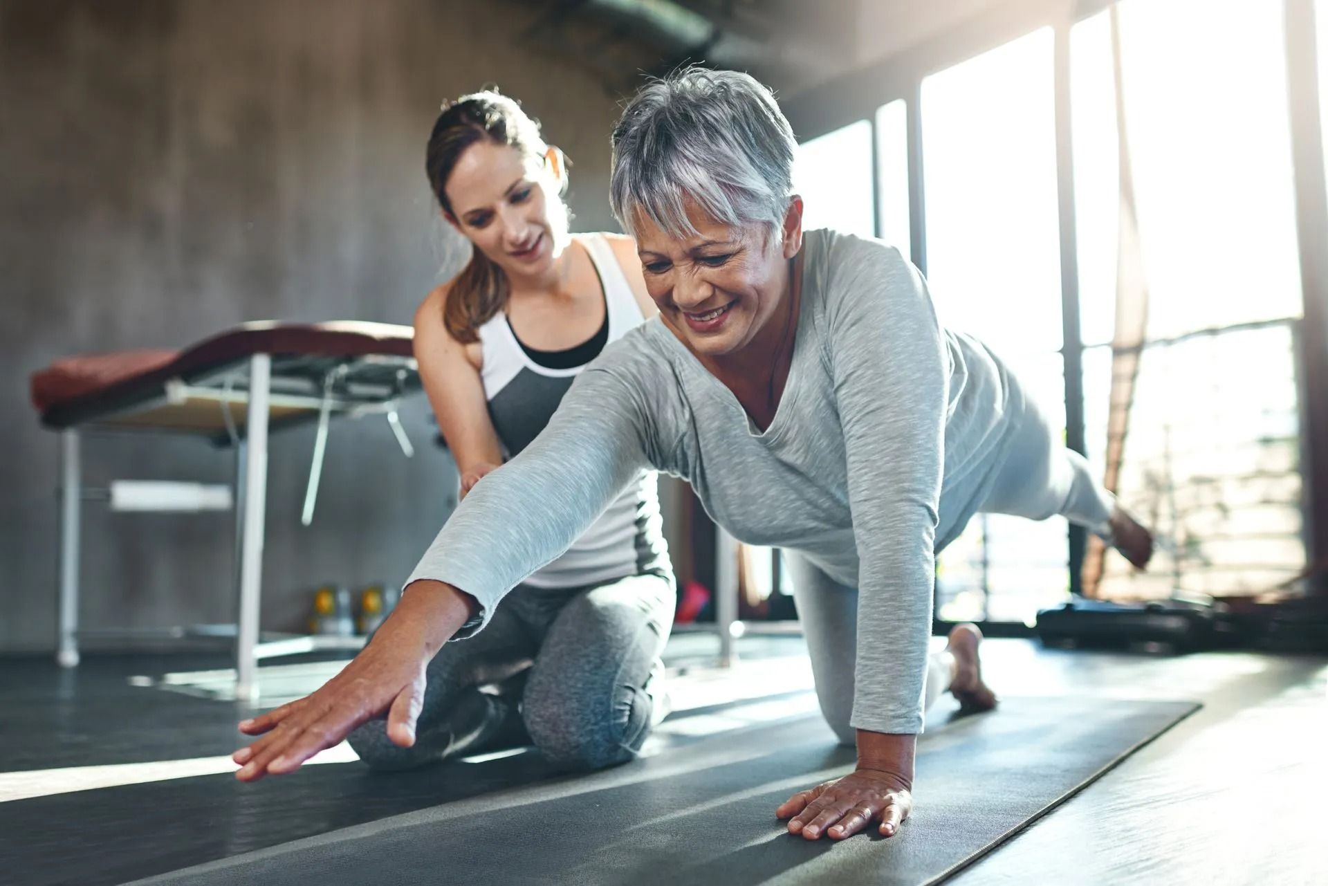 A woman is helping an older woman do push ups on a yoga mat.