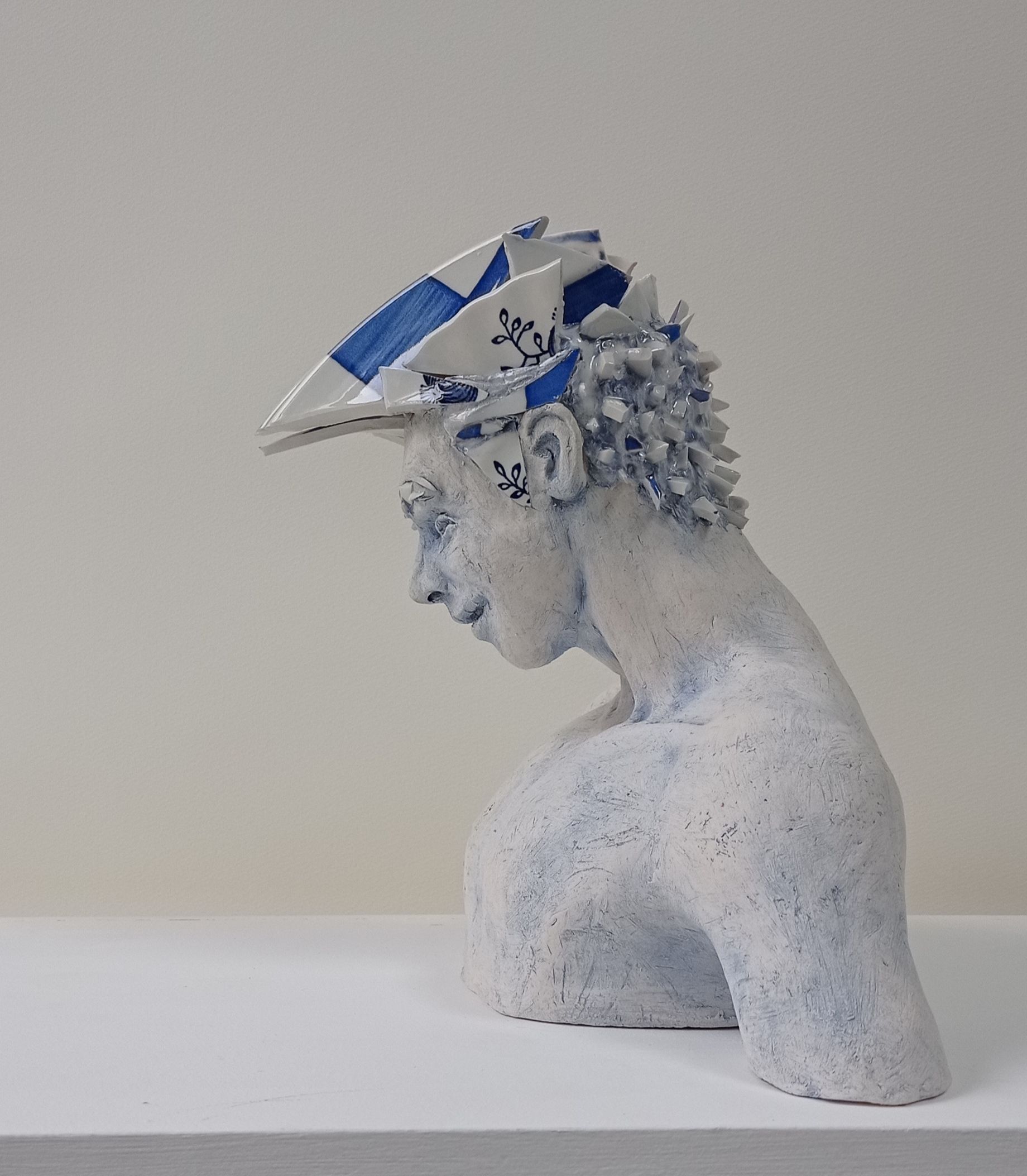 White ceramic bust of a person wearing a blue and white tile hat, looking down.