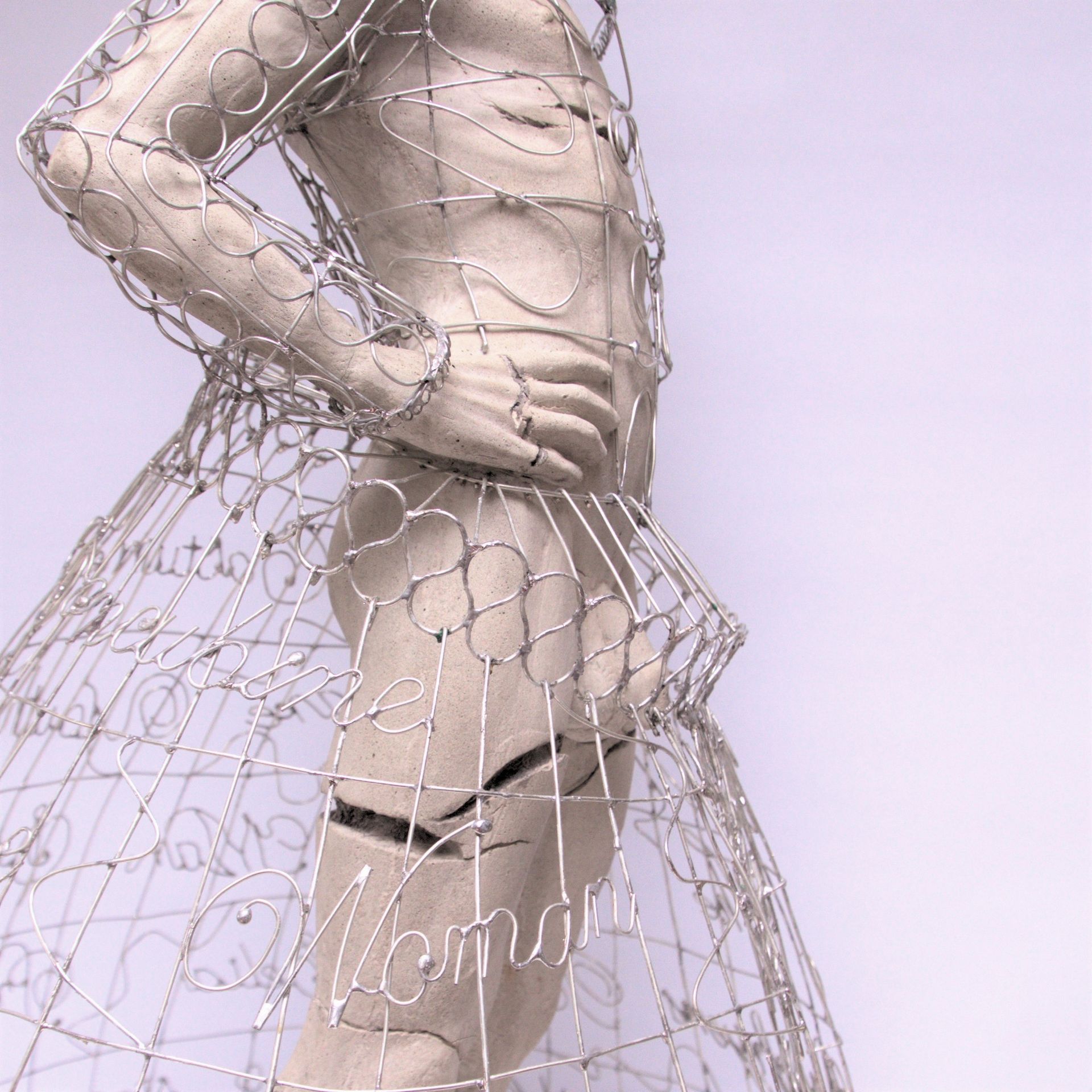 Wire sculpture of a person, torso visible, wearing a cage-like skirt, hand on hip.