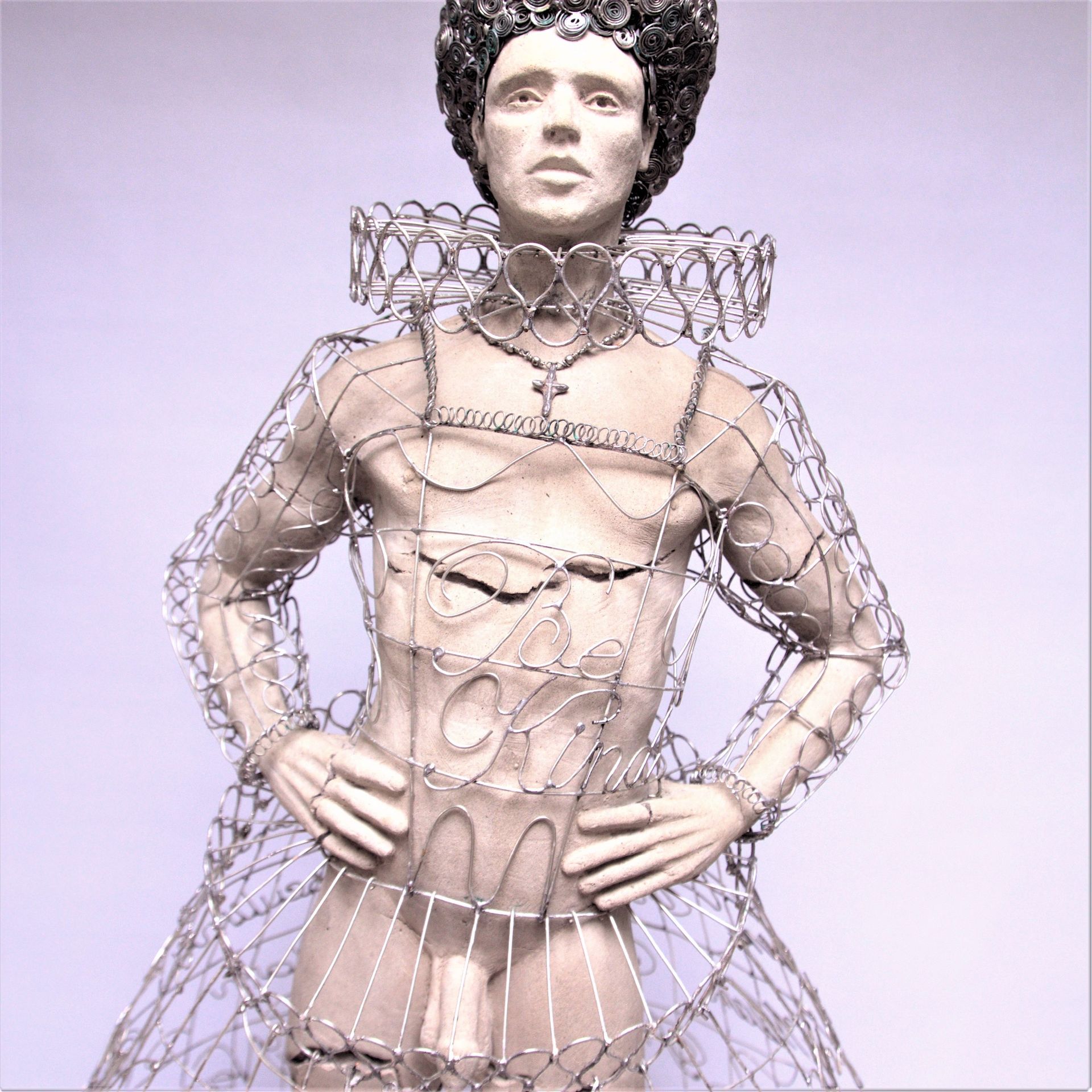 Wire sculpture of a person in Elizabethan attire with hands on hips, stern expression.