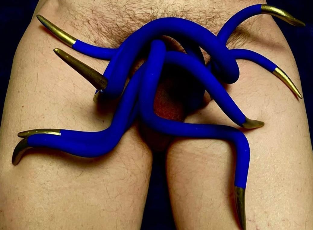 Blue and gold, tentacle-like prosthetic over groin. Light skin background.