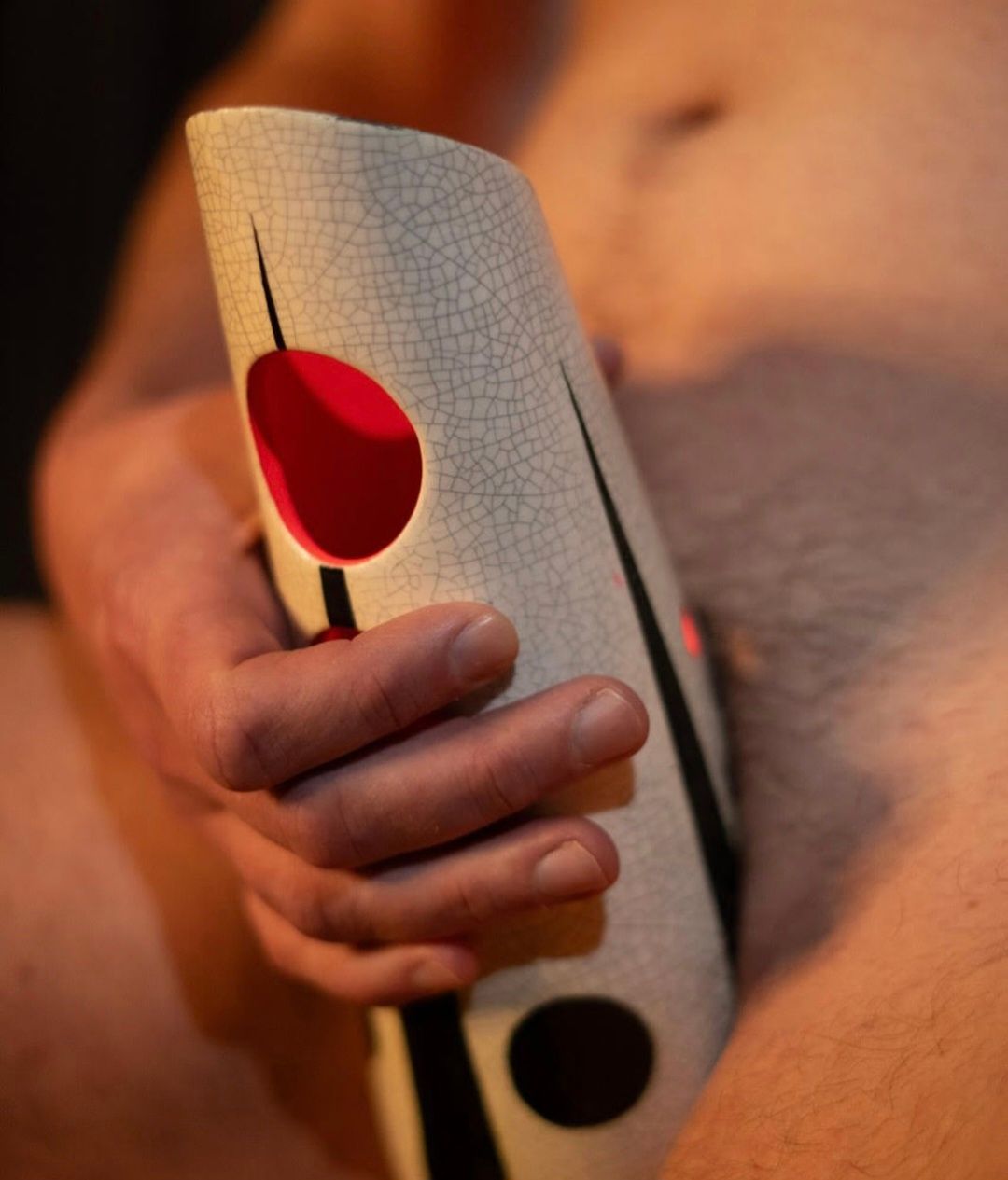 A man holding a patterned paper in front of his body, red and black circles, beige background.
