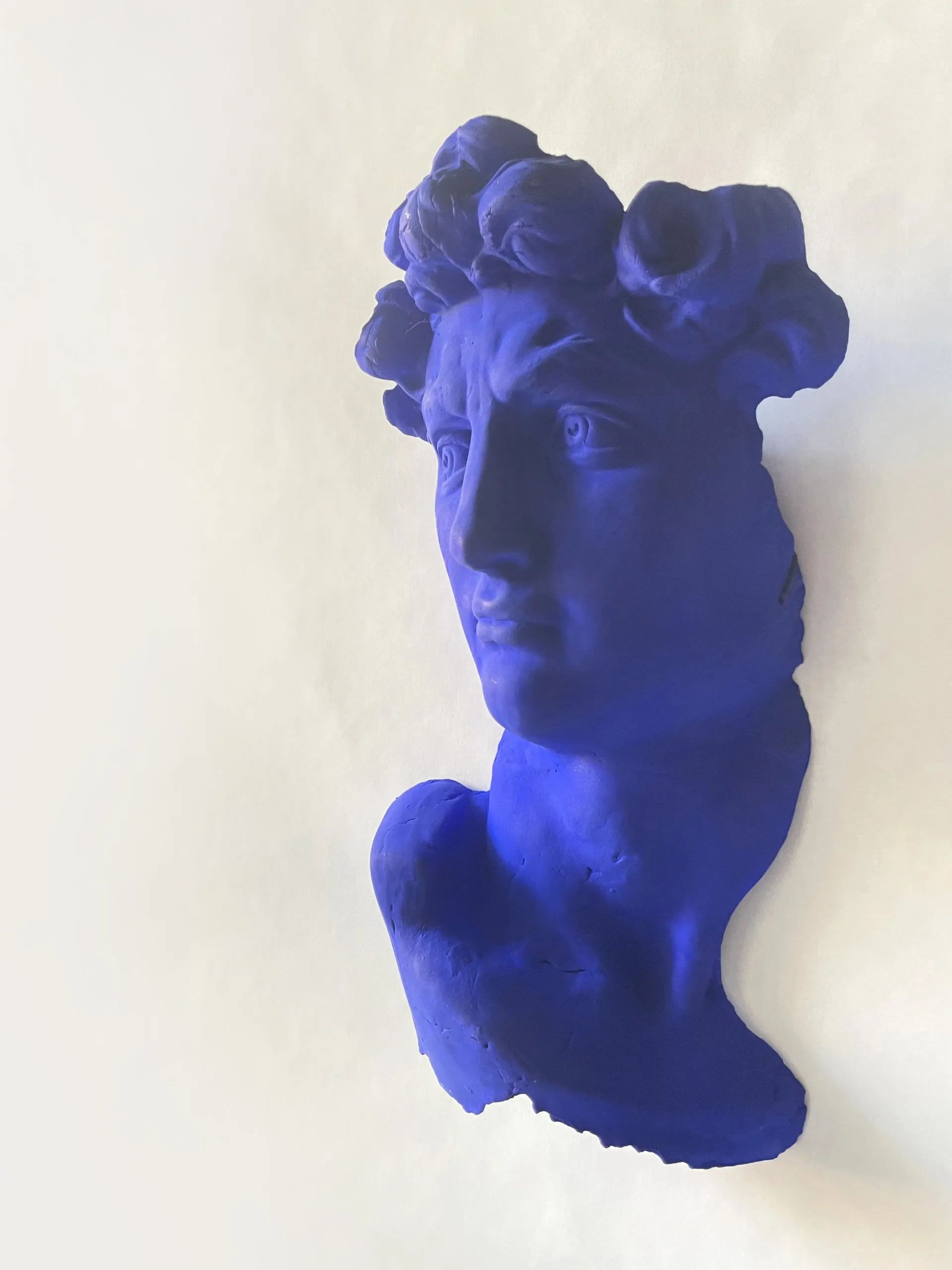 Blue sculpture of a classical bust, with elaborate hair, set against a white backdrop.