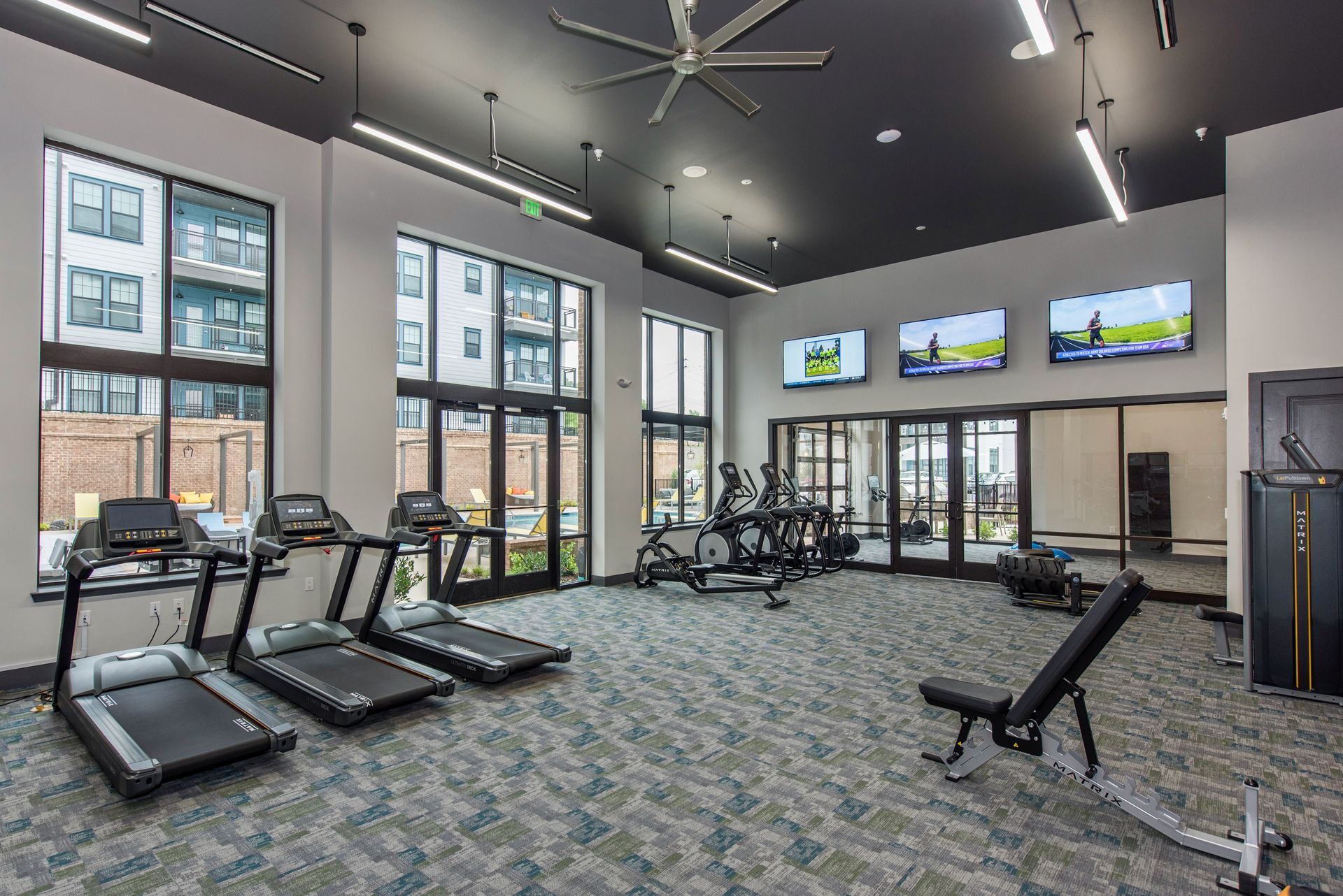 A large gym with treadmills, a bicycle, a bench, and a ceiling fan.
