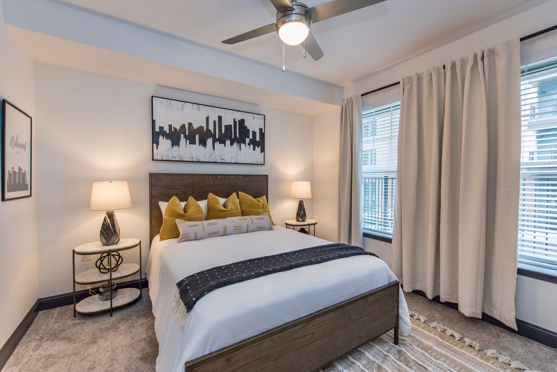 A bedroom with a king-size bed, two nightstands, a ceiling fan, and two windows.