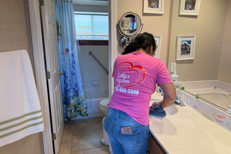 A woman in a pink shirt is cleaning a bathroom sink.