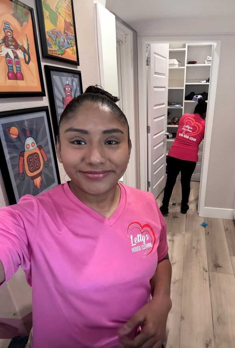 A woman in a pink shirt is taking a selfie in a hallway.