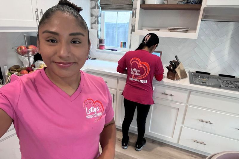 A woman in a pink shirt is taking a selfie in a kitchen.