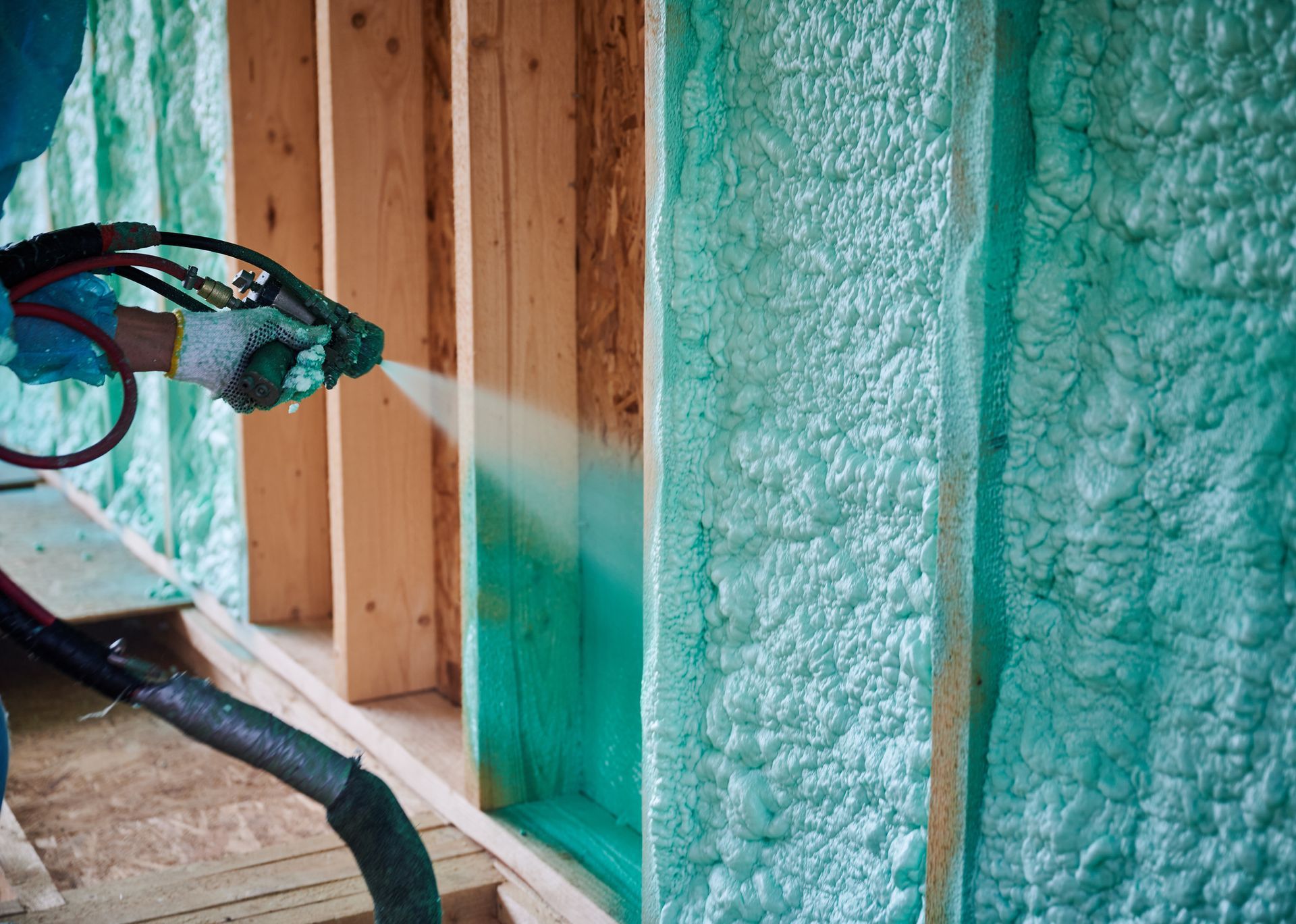 A person is spraying foam insulation on a wall.