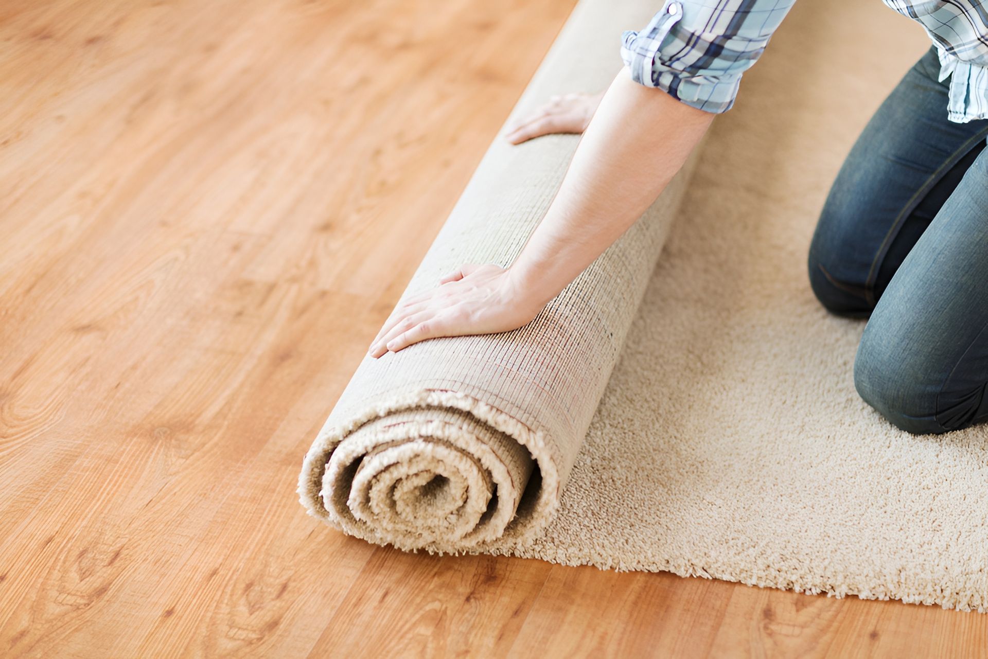 Person Rolling Out a Beige Carpet on a Wooden Floor — Kingaroy Carpet Cleaners in Kingaroy, QLD