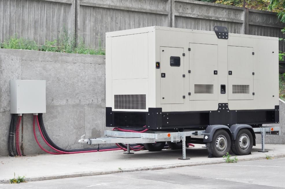 Generator on trailer next to wall, wires connecting it to a utility box.