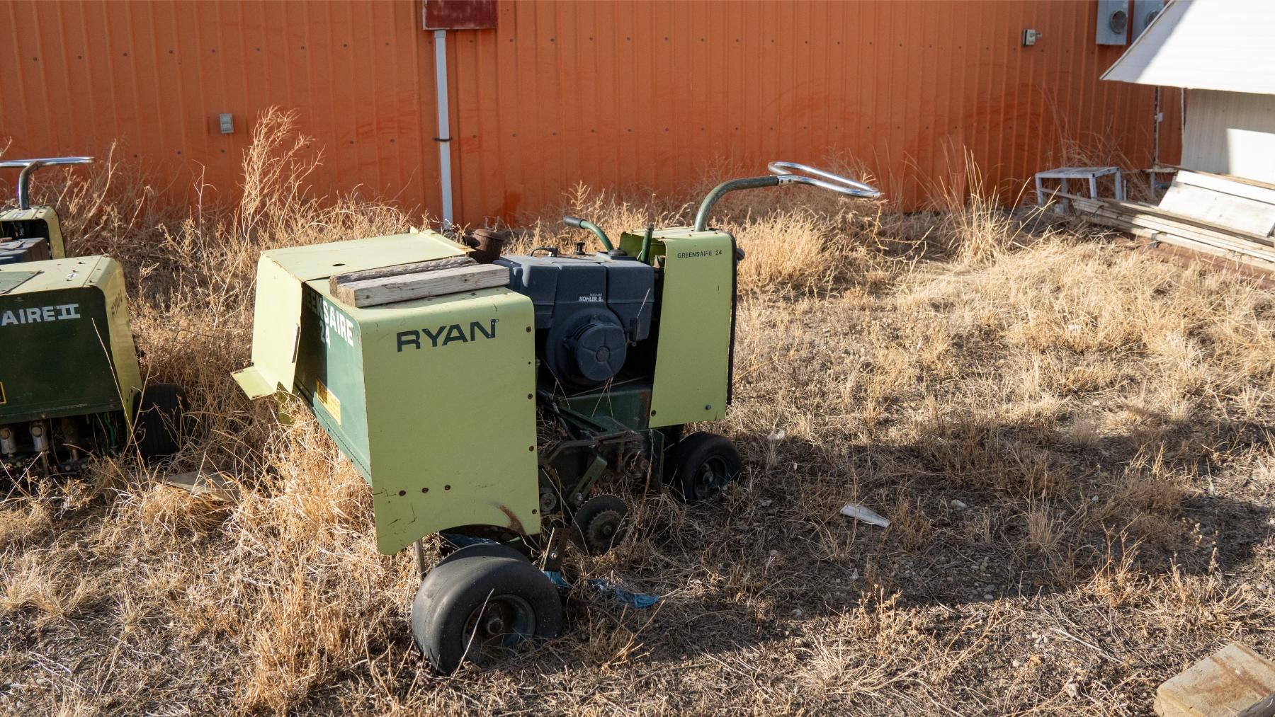 Ryan lawn aerator in a grassy area with an orange building in the background.