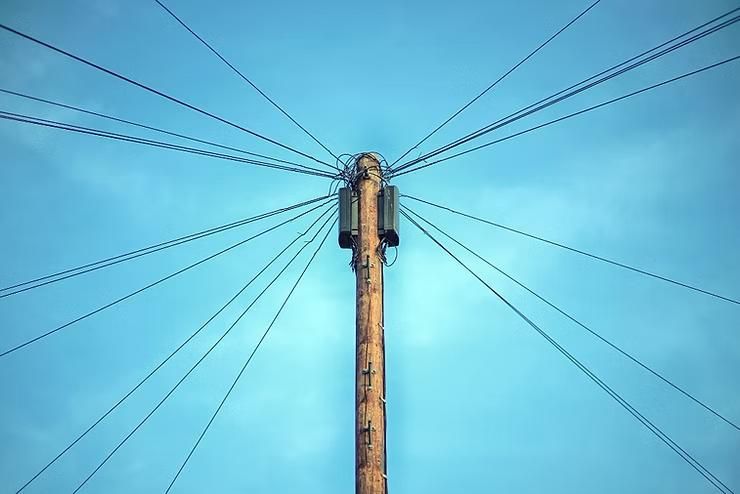 A wooden pole with lots of wires attached to it against a blue sky.