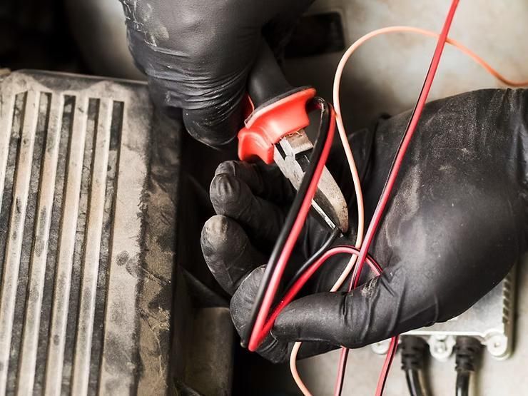 A person wearing black gloves is holding a pair of pliers and a bunch of wires.