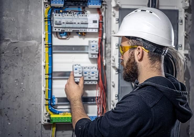A man wearing a hard hat and goggles is working on an electrical box.