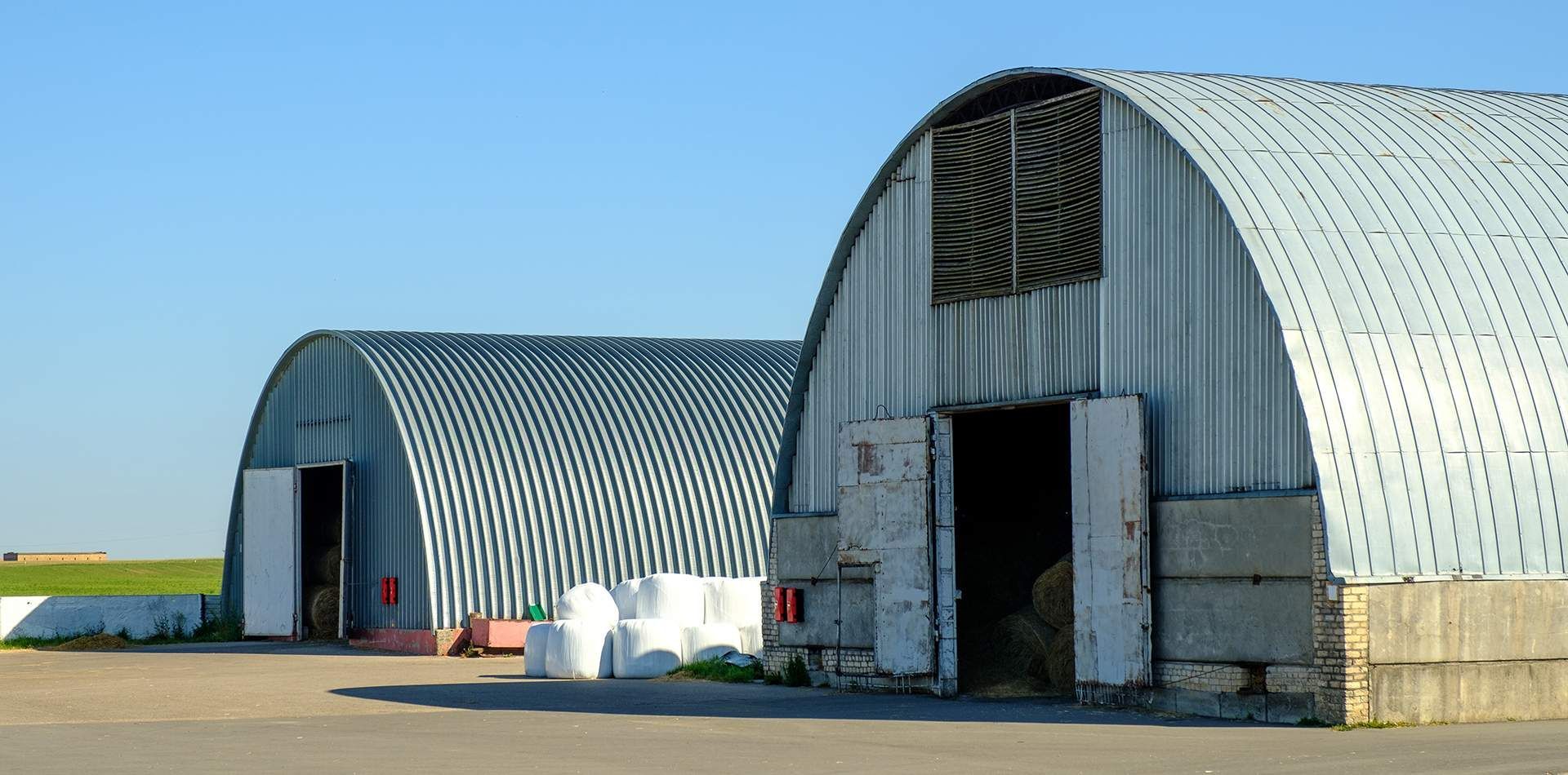 Two large metal buildings are sitting next to each other in a field.