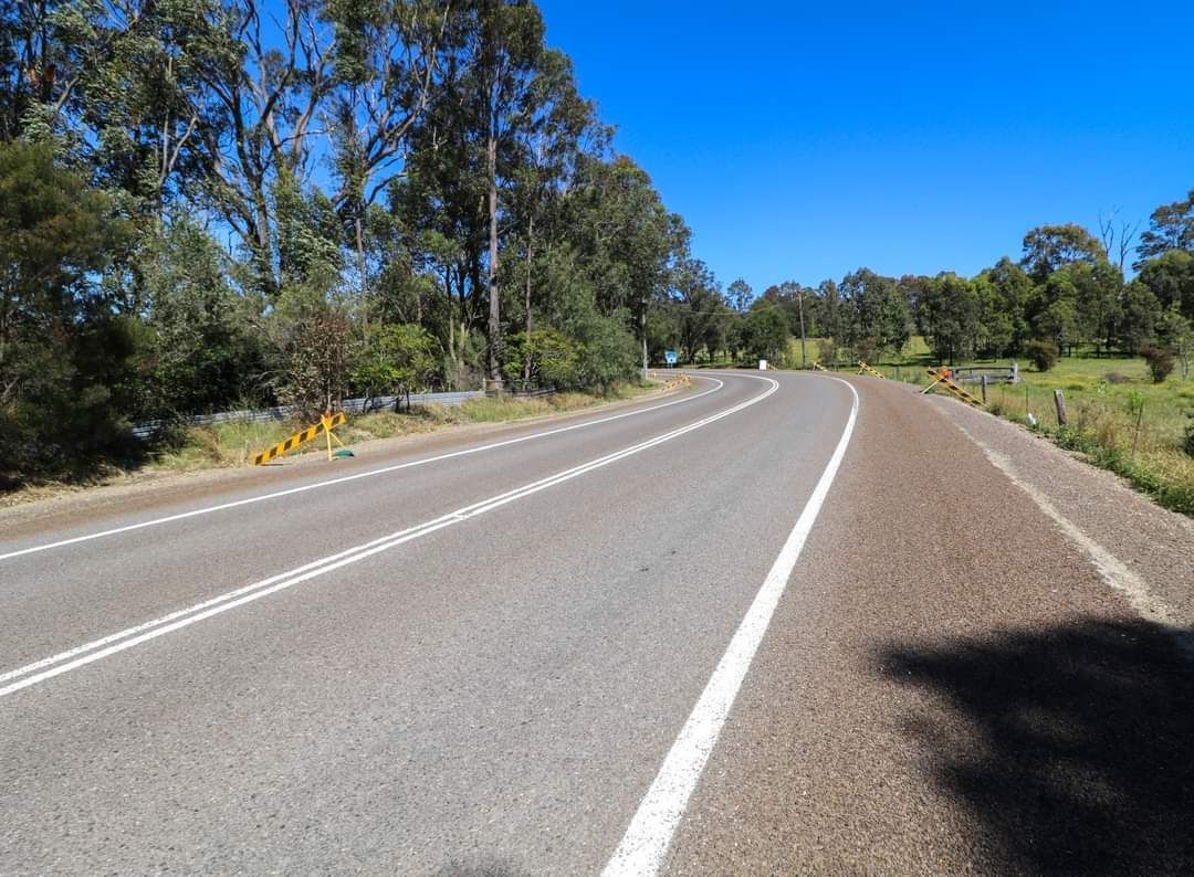 An empty highway with trees on both sides and a blue sky in the background.